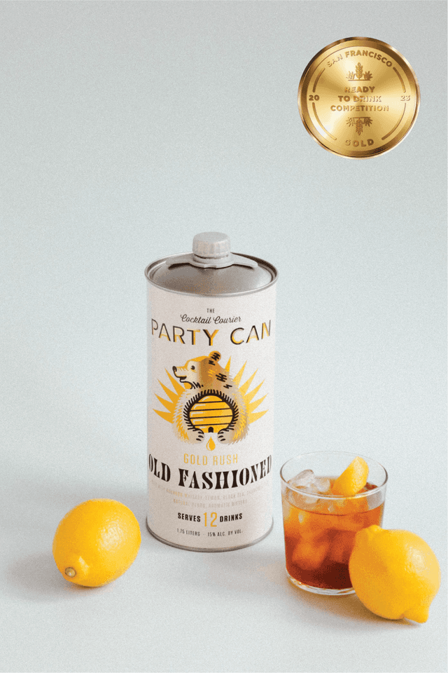 Party Can Gold Rush Old Fashioned can next to the cocktail in a glass with ice.